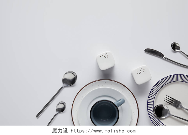 白色桌子上的餐具盐瓶, 胡椒脚轮, 勺子, 刀, 叉子, 杯和盘子在白色桌上的顶部视图